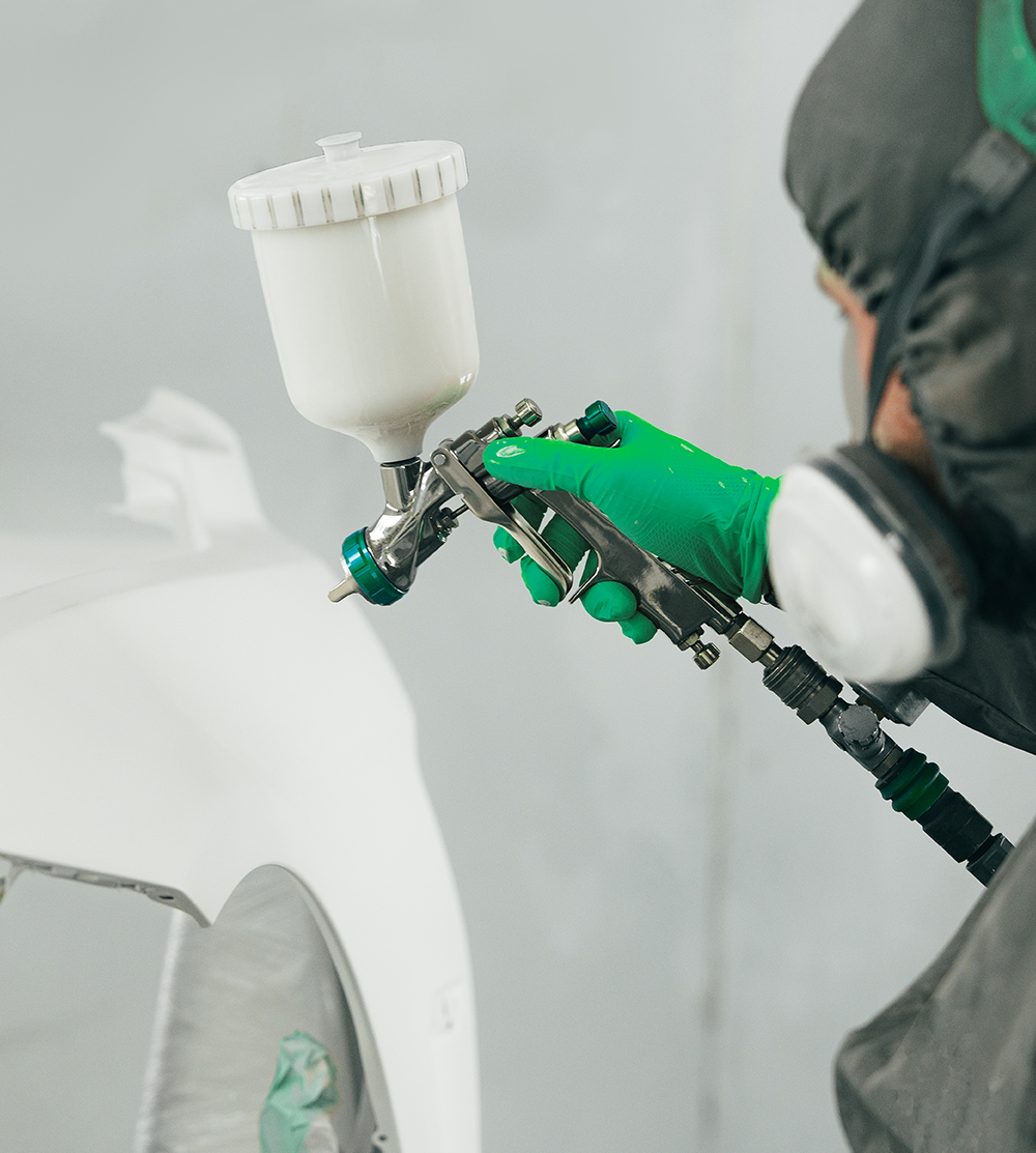 Lackierer trägt frische Lackschicht mit Lackierpistole auf Fahrzeugoberfläche in Steyr auf
