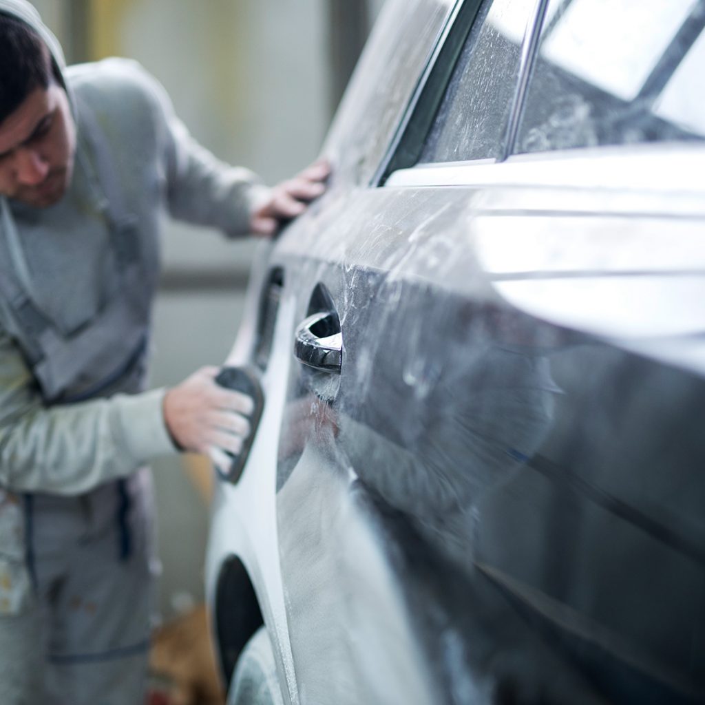 Facharbeiter schleift beschädigte Fahrzeugstelle zur Reparaturvorbereitung in der Werkstatt in Steyr