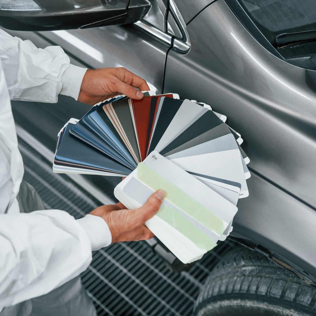 Hand hält Farbfächer zur Farbtonberatung an Fahrzeugoberfläche in Steyr