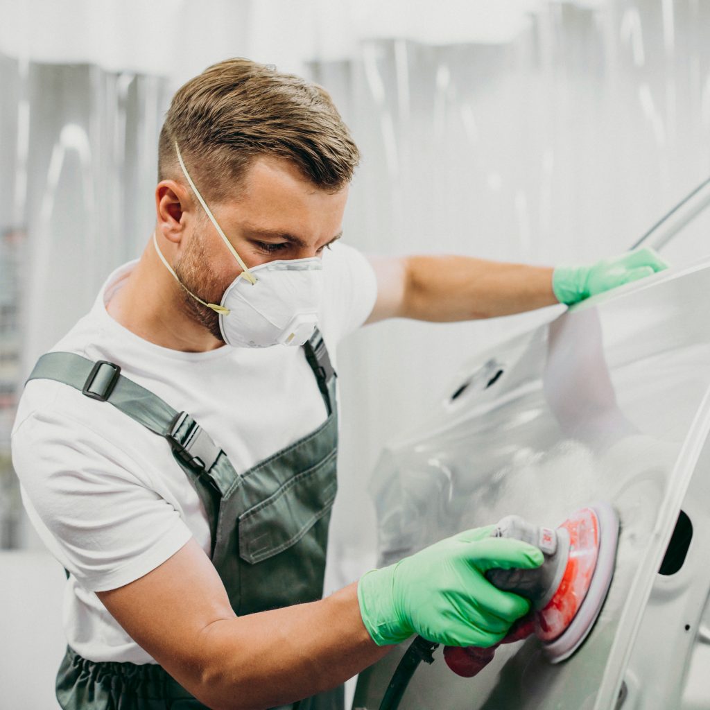 Facharbeiter schleift Fahrzeugkarosserie zur Vorbereitung auf Reparatur und Lackierung in Steyr