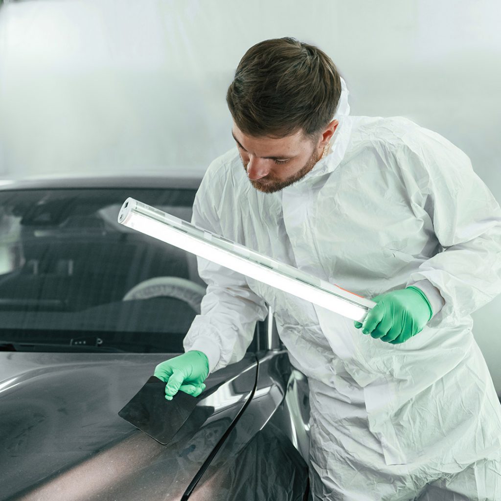 KFZ Lackierer bei der Prüfung und Vorbereitung einer Fahrzeugoberfläche in der Werkstatt in Steyr